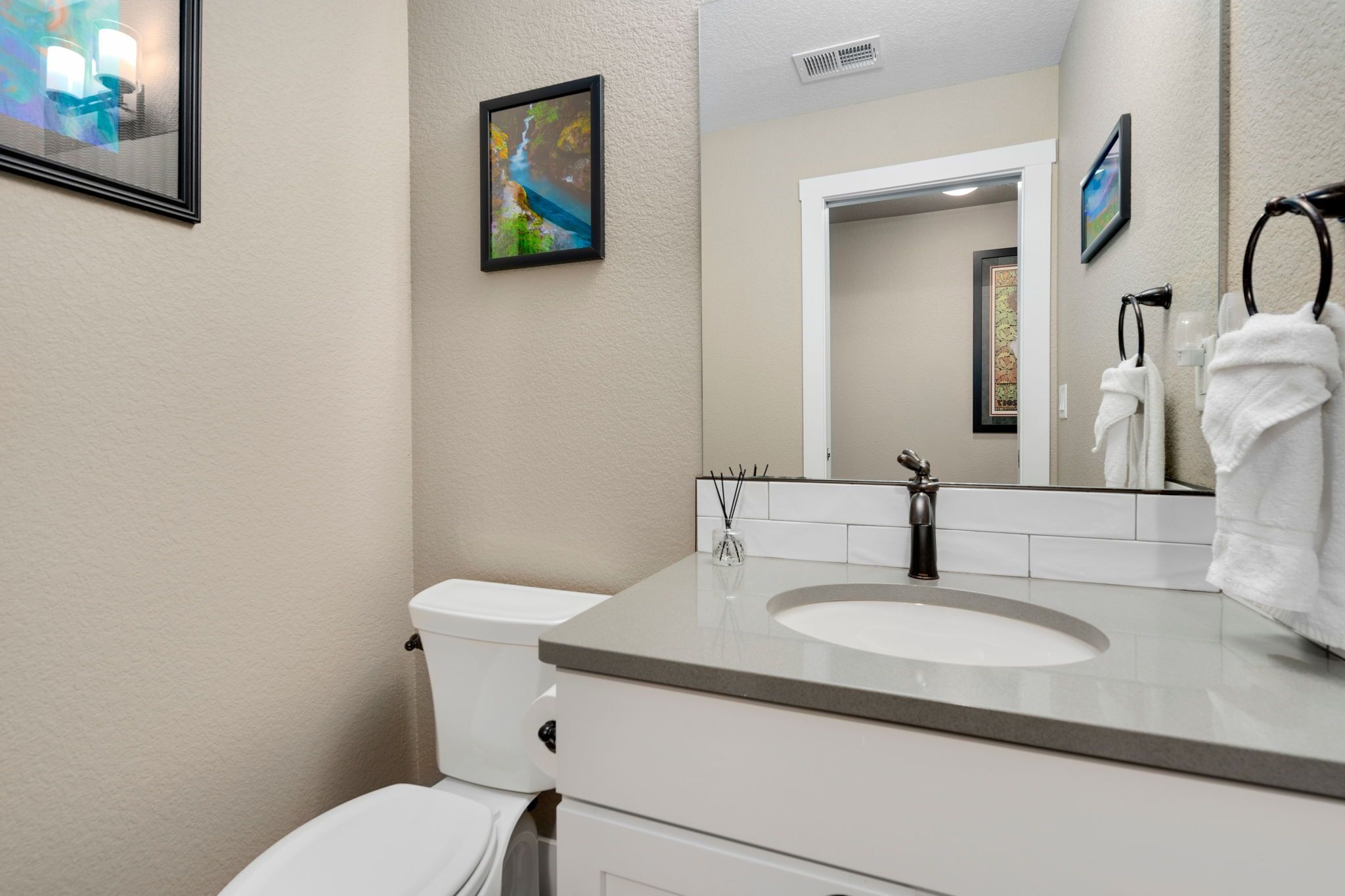 Een moderne badkamer met een wit toilet, een wastafel en een spiegel. Er hangen twee afbeeldingen in lijsten aan de muur.