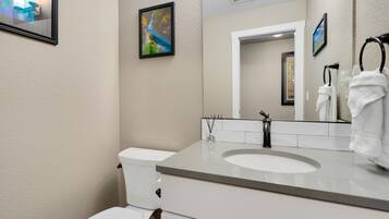Een moderne badkamer met een wit toilet, een wastafel en een spiegel. Er hangen twee afbeeldingen in lijsten aan de muur.