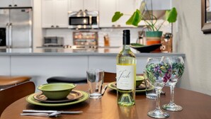 A dining table with a bottle of wine, two glasses, a bowl, and cutlery.