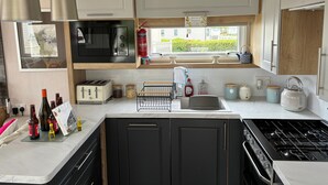 Une cuisine compacte équipée d’un four à micro-ondes, d’un grille-pain, d’un évier et d’une cuisinière. Une fenêtre offre une vue sur la verdure environnante.