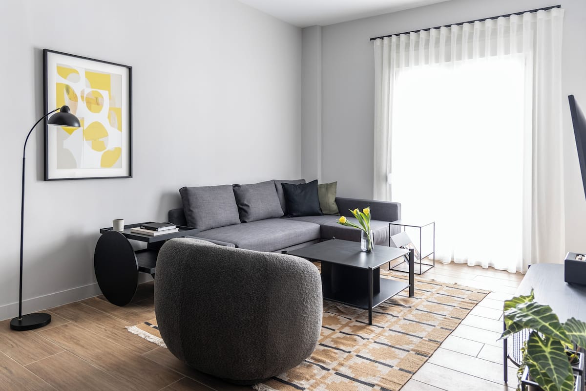 Ein modernes Wohnzimmer mit einem grauen Sofa, einem runden Sessel, einem Couchtisch und einer Stehlampe.