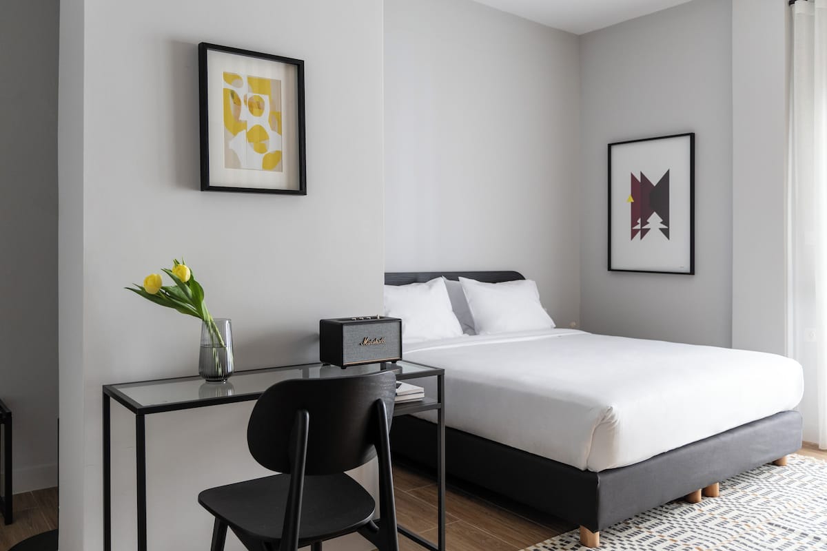 Ein modernes Hotelzimmer mit einem Bett, einem Schreibtisch mit Stuhl und einer Vase mit Blumen.