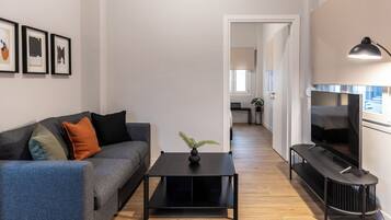 A modern living room with a sofa, a coffee table, and a TV. There is a framed picture on the wall and a plant on the coffee table.