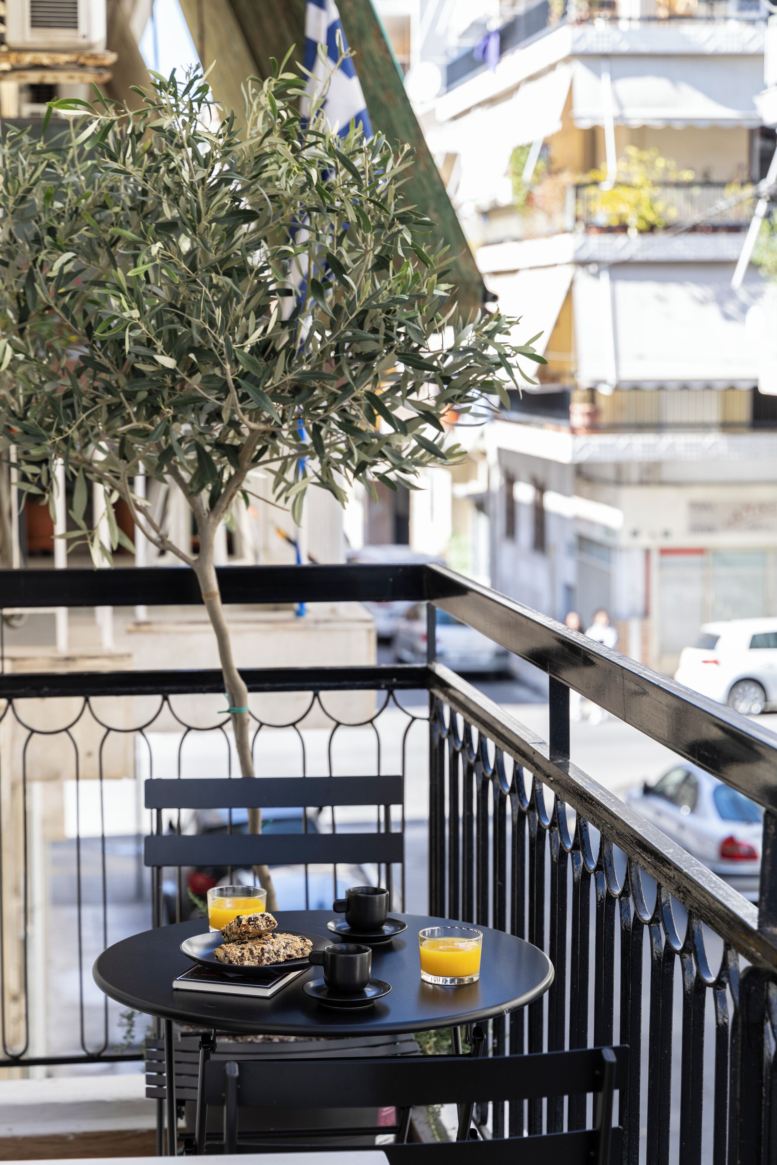 A balcony with a table set for breakfast, including a plate of cookies, a glass of orange juice, and a cup.