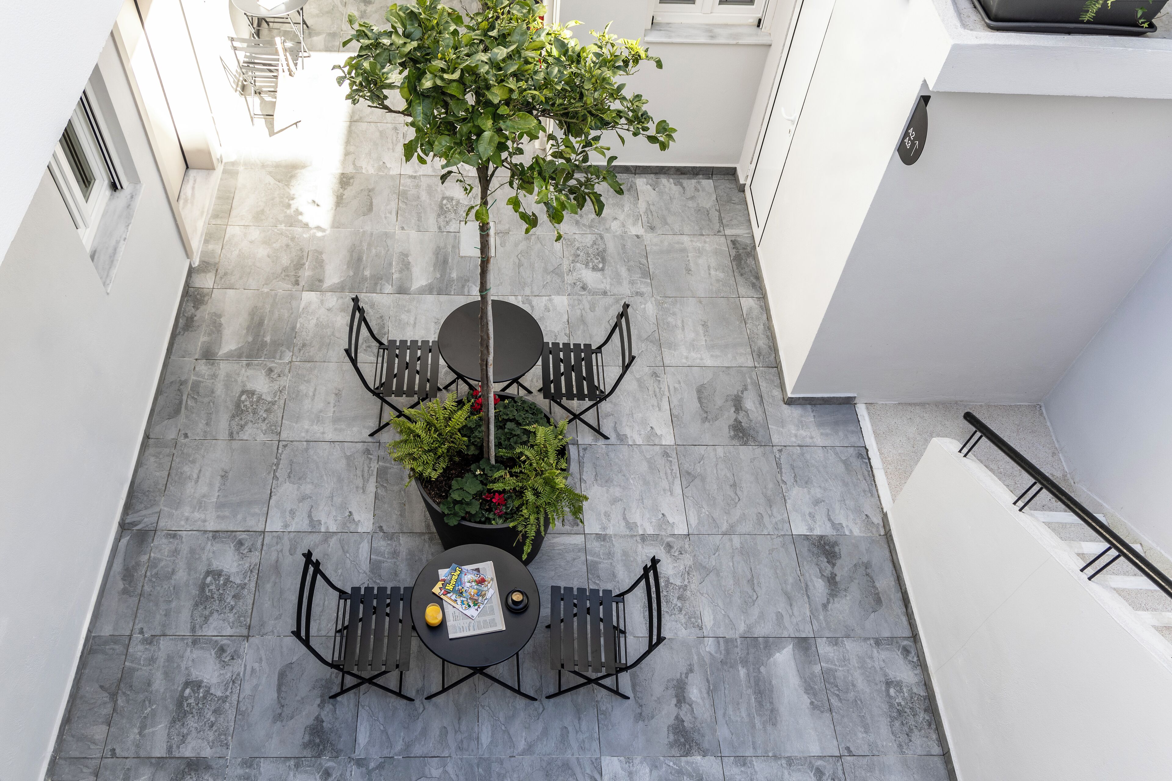 Um pátio externo com duas mesas redondas e cadeiras, um vaso de planta e uma escadaria.