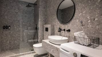 A modern bathroom with a freestanding toilet, a sink with a marble countertop, a large mirror, and a washing machine.
