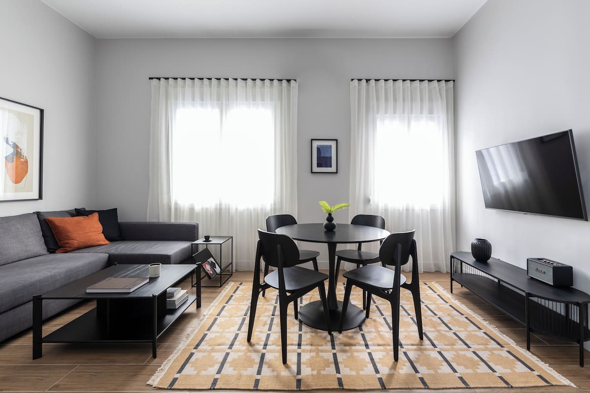 Ein modernes Wohnzimmer mit einem grauen Sofa, einem runden Esstisch mit Stühlen, einem Couchtisch und einem flachbildfernseher an der Wand.