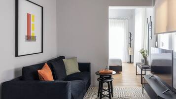 A modern living room with a black sofa, a small round table, and a large flat-screen TV.