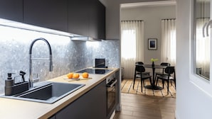 A modern kitchen with a large island, dark cabinets, and a dining area with a table and chairs. - Elliot Petralona, Athens (Athens)