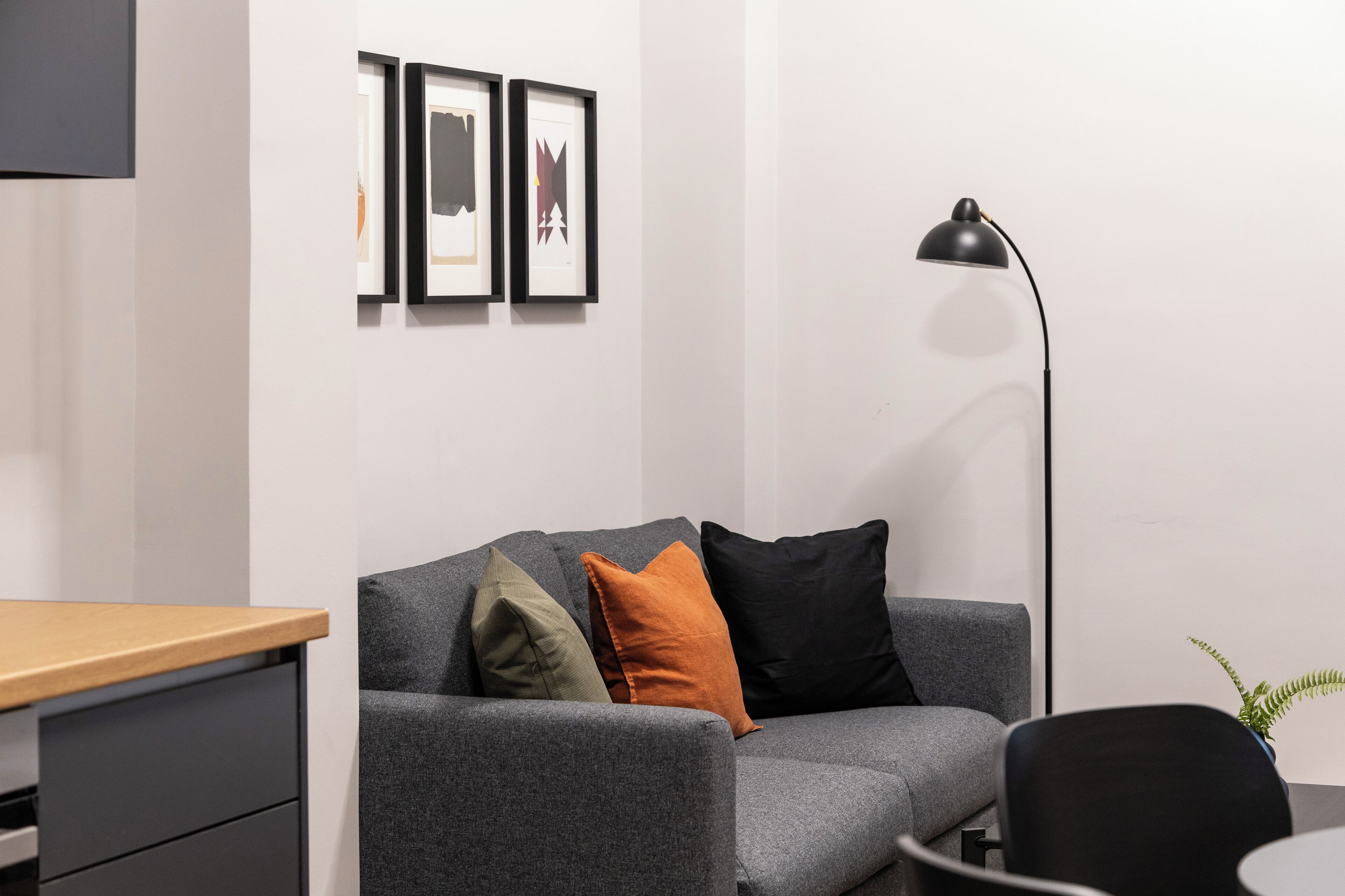 A modern office space with a grey sofa, a wooden desk, and a black floor lamp.