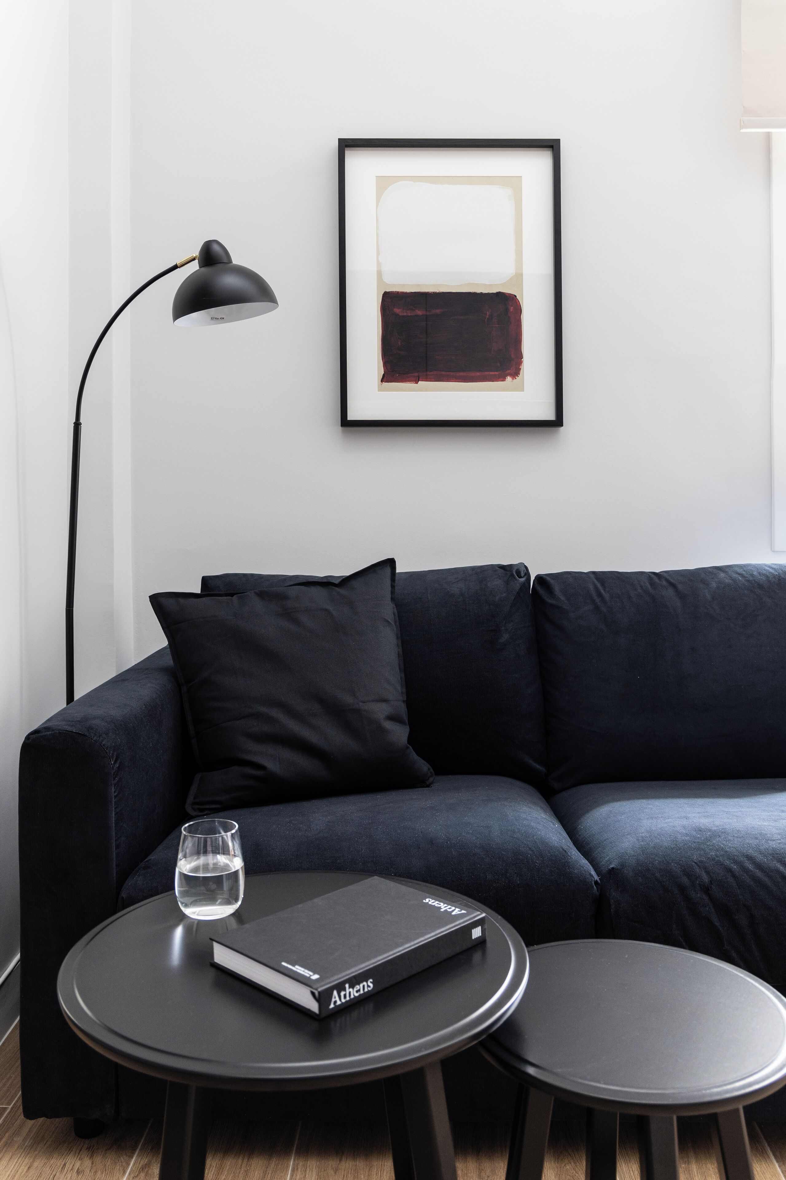 A modern living room with a dark sofa, a round coffee table, a framed abstract painting, and a floor lamp.