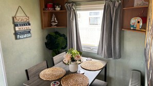 A cozy room with a wooden table, woven placemats, a potted plant, and a shelf with books and decorative items. - 6 Berth Caravan Next To The Beach-ingoldmells-dog Friendly (Skegness)