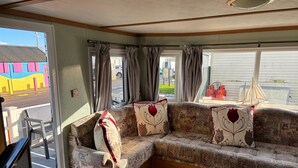 A corner sofa with patterned cushions, a view of the street, and a small sailboat model on a table. - 6 Berth Caravan Next To The Beach-ingoldmells-dog Friendly (Skegness)