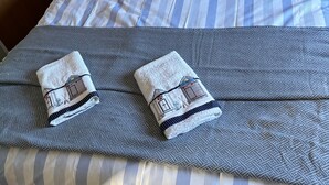 A neatly made bed with striped bedding, two pillows with text, a lamp, and folded towels on a gray blanket. - 6 Berth Caravan Next To The Beach-ingoldmells-dog Friendly (Skegness)