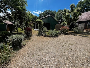 A gravel driveway leading to a green building with a sloped roof, surrounded by trees and shrubs. - Verdier, Gîte with shared swimming pool in Dordogne (Saint-Avit-Sénieur)