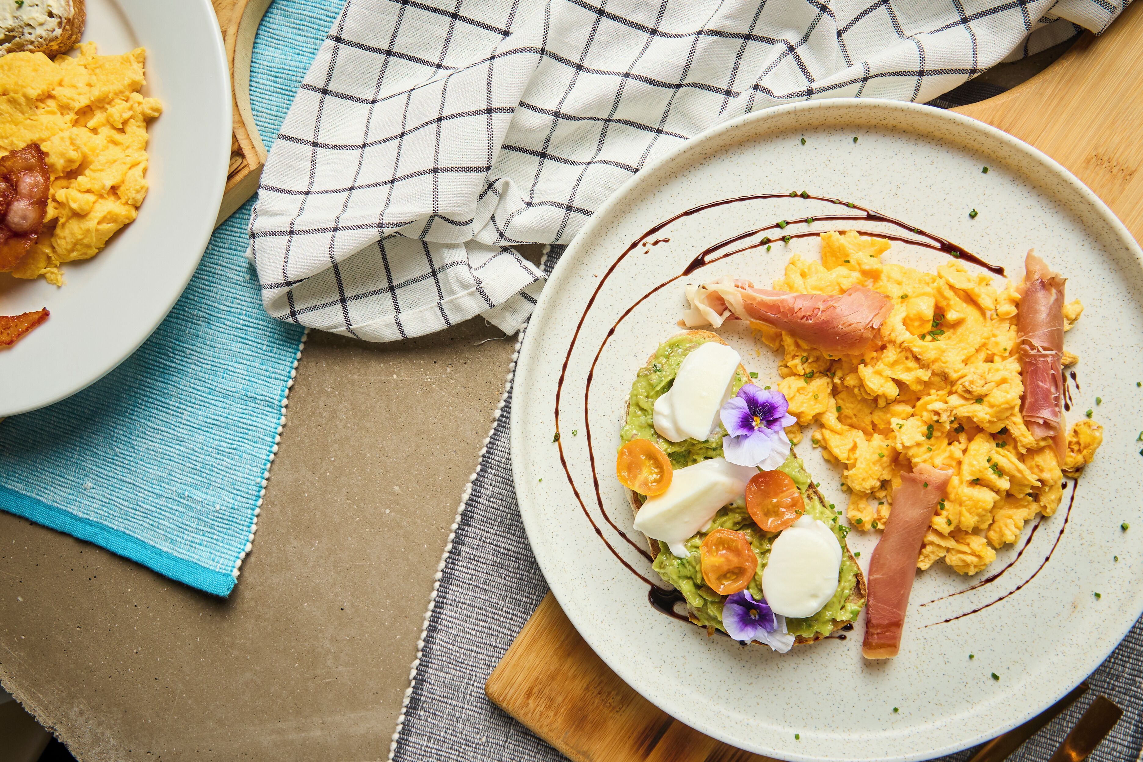 A plate of scrambled eggs with bacon, avocado, and a poached egg on a ceramic plate.