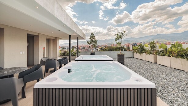 Een terras op het dak met twee jacuzzi's, een eethoek met stoelen en een tafel, en uitzicht op een stadsbeeld met bergen op de achtergrond.