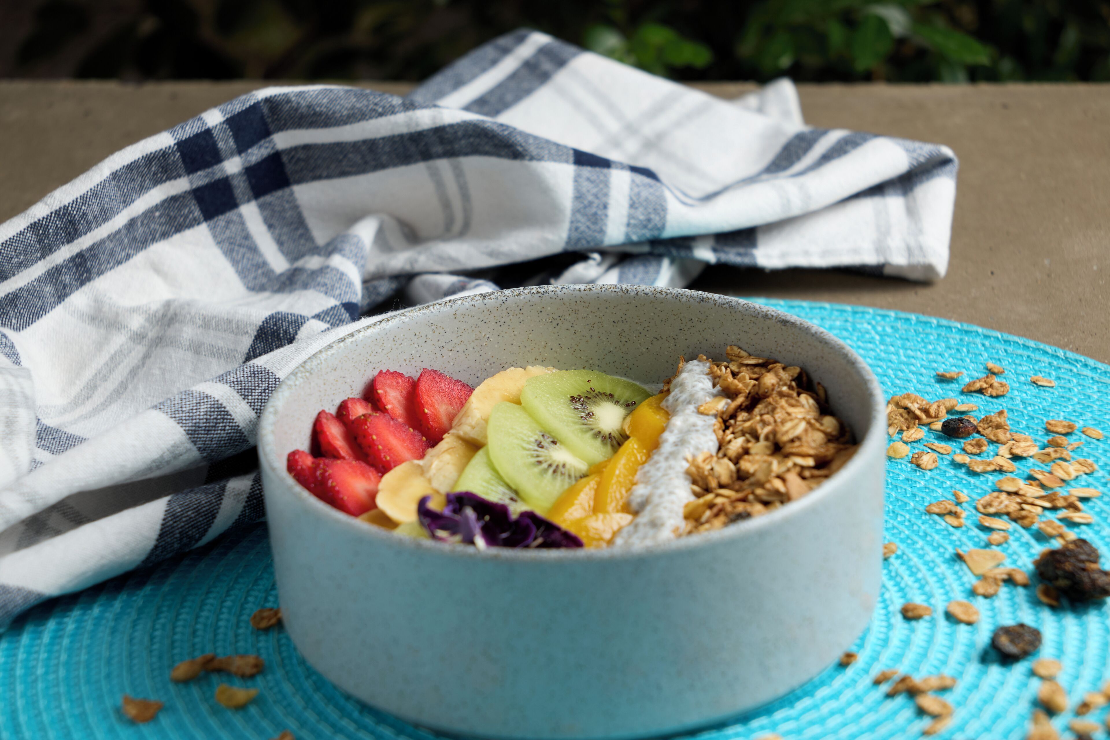 Een schaal met fruit en granola op een blauwe placemat.