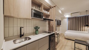Een moderne keuken met een ingebouwde magnetron, een spoelbak en een klein aanrecht. Een televisie is aan de muur bevestigd en in de aangrenzende kamer staat een bed met een raam.