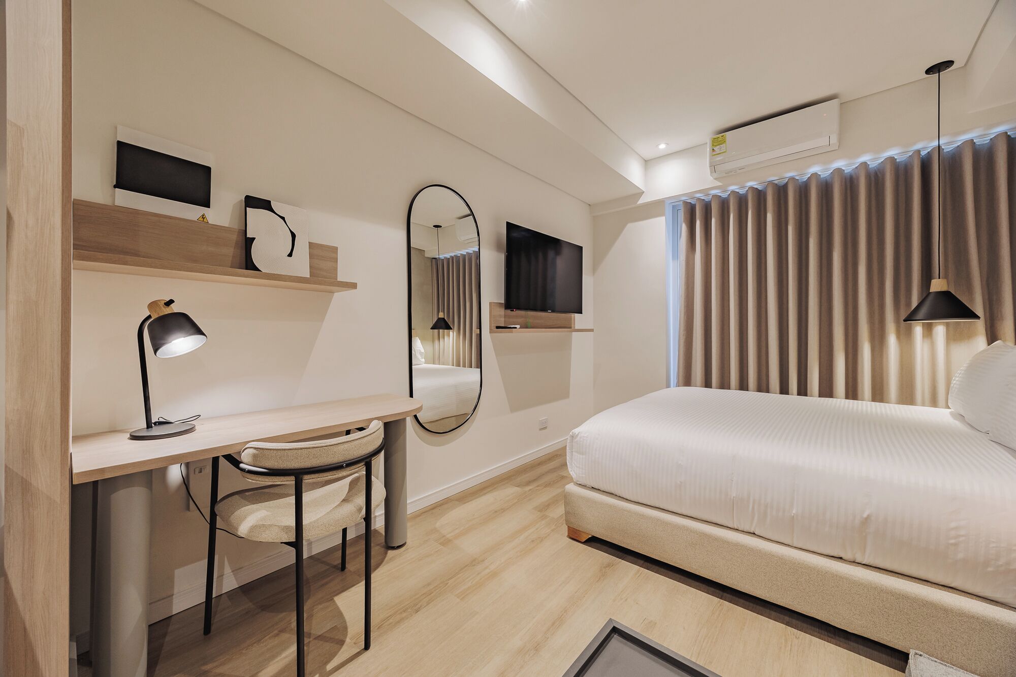 Moderni hotellihuone, jossa on sänky, työpöytä, tuoli ja suuri peili.