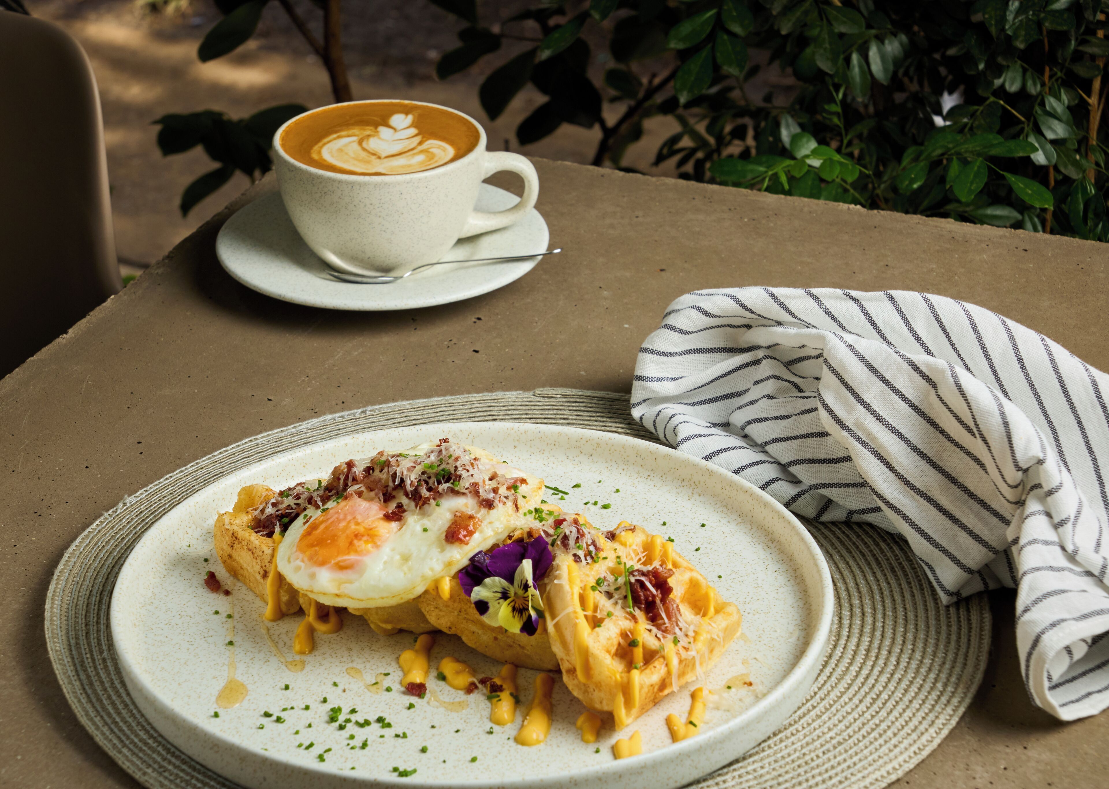 Ein Teller mit Essen, darunter ein Spiegelei und Käse, eine Tasse Kaffee sowie ein gestreiftes Servietten.