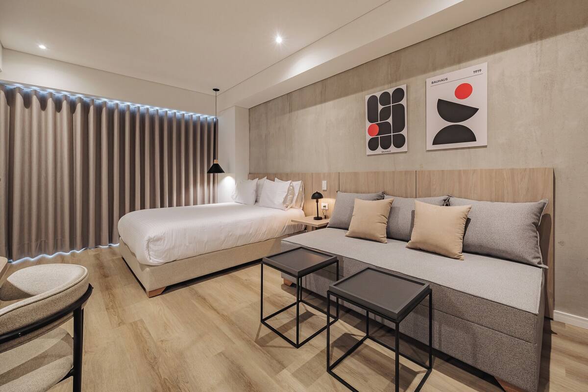 Habitación de hotel moderna con cama, sofá y dos mesas.