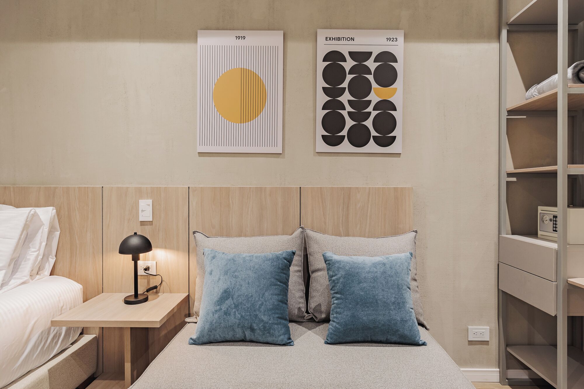Une chambre à coucher avec une tête de lit en bois, une table de chevet avec une lampe, deux oreillers et deux œuvres d’art encadrées accrochées au mur.