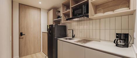 Una cocina compacta con un refrigerador negro, un microondas y una cafetera.