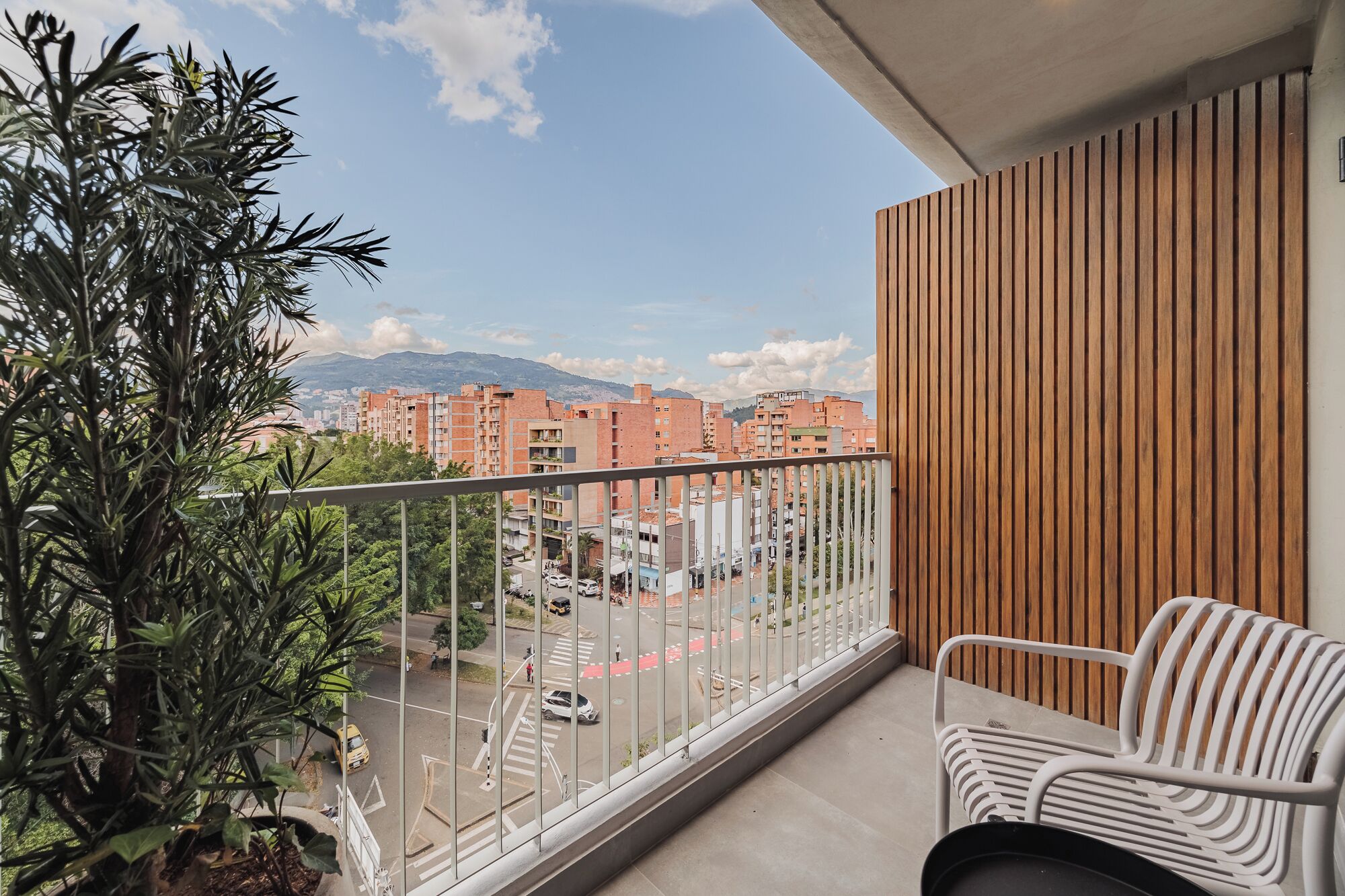 A balcony with a view of a cityscape, a wooden wall, and a white chair.