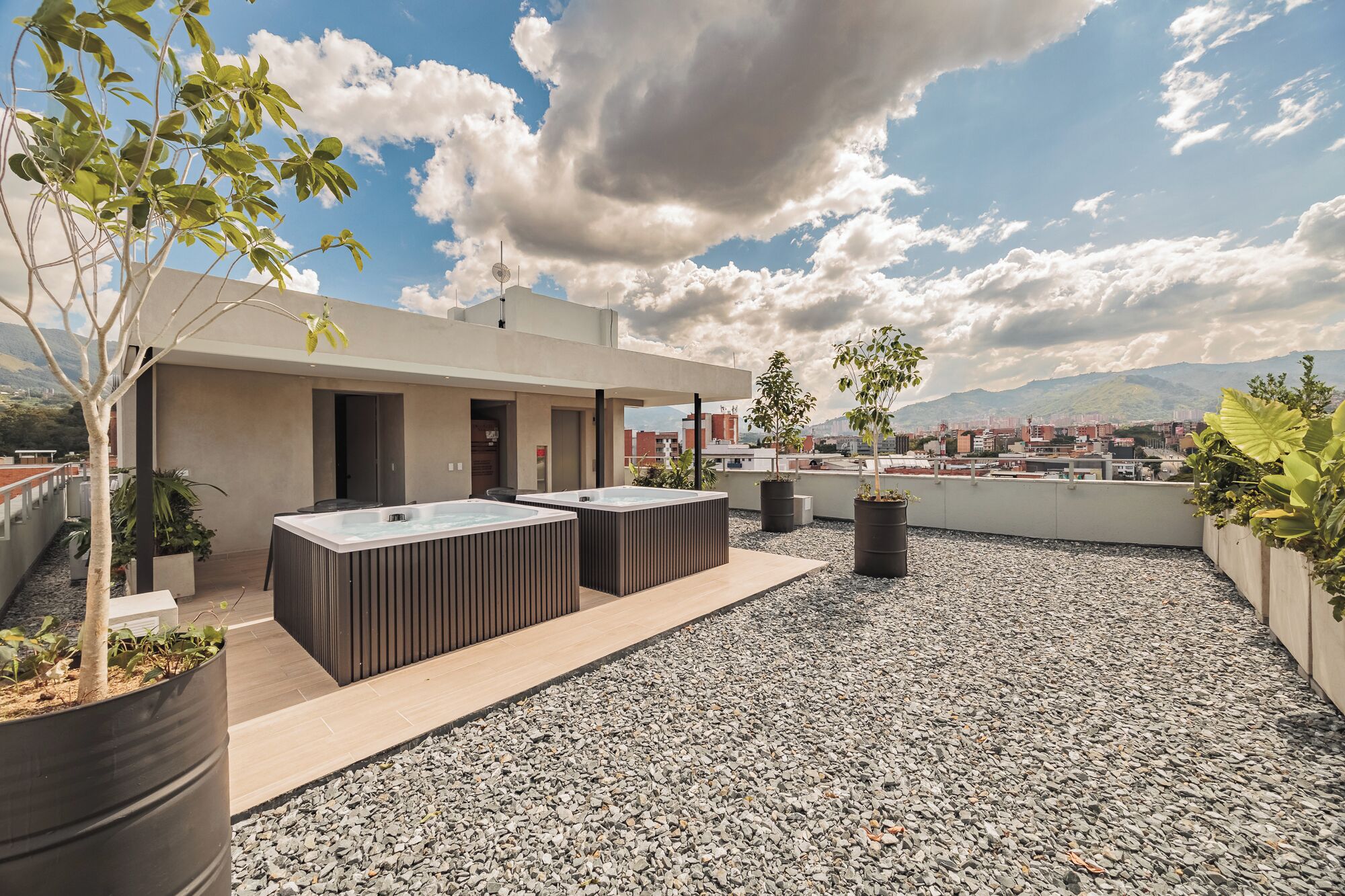 Terraza en la azotea con dos jacuzzis, plantas en macetas y vistas a la ciudad y las montañas.