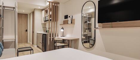A modern hotel room with a large bed, a desk with a chair, a wardrobe, a mirror, and a TV mounted on the wall.