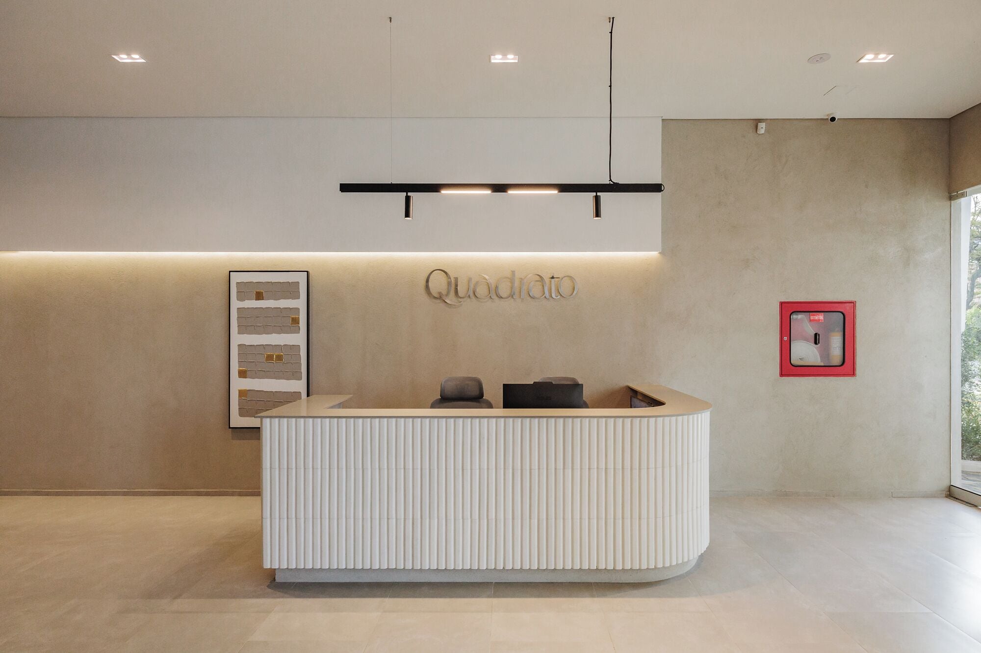 A reception desk with a modern design, a wall-mounted sign reading "Quadrato", and a framed artwork to the left.
