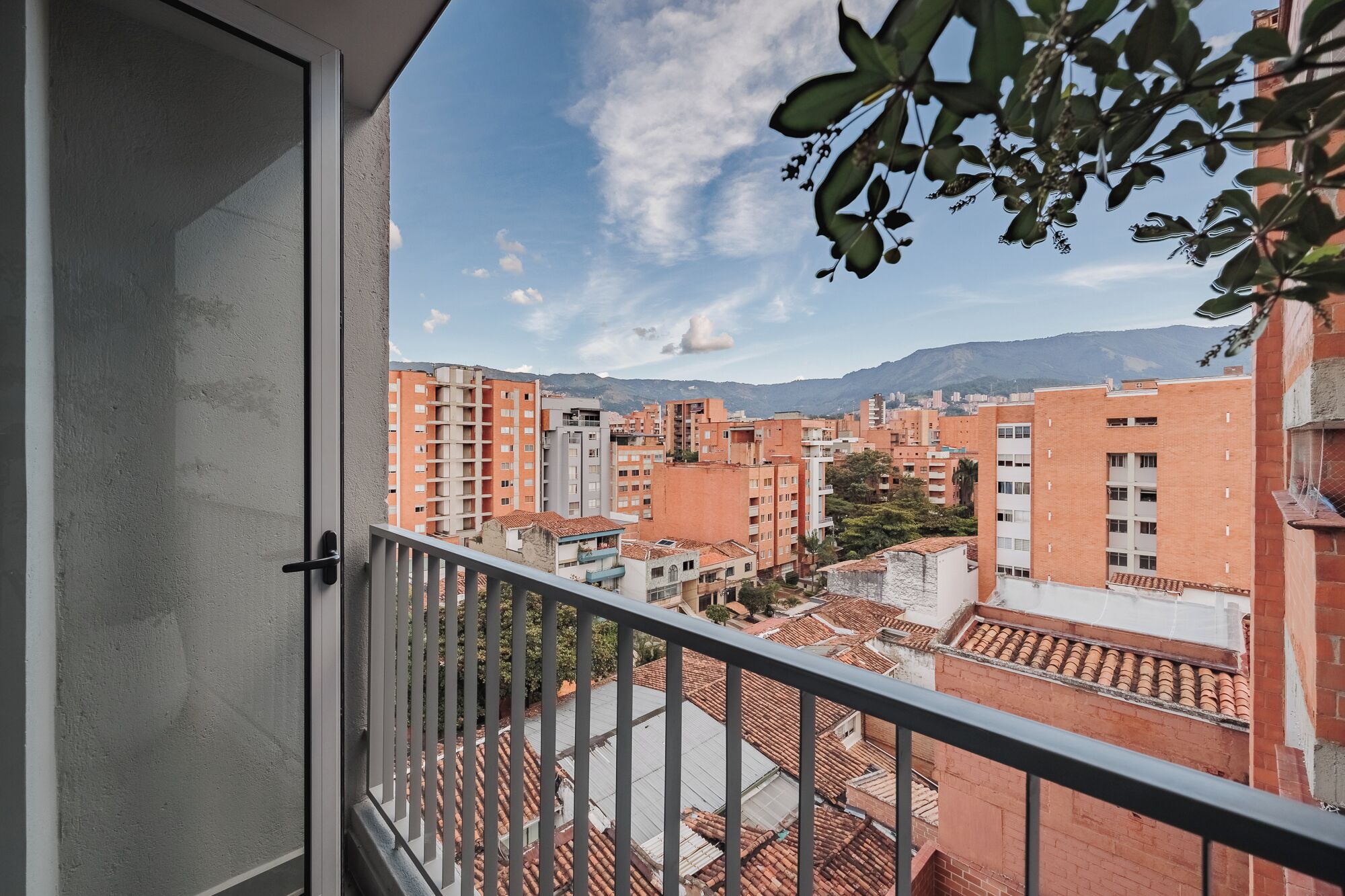 Un balcon offrant une vue sur le paysage urbain, avec des bâtiments aux toits rouges et une montagne en arrière-plan.