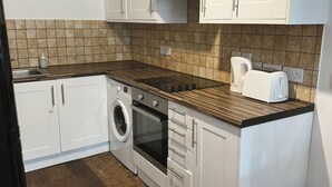 A kitchen with white cabinets, a built-in oven, a washing machine, and a wooden countertop. - Cosy One Bedroom London Apartment (London)