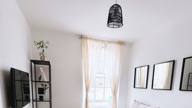 A modern living room with a sofa, a glass coffee table, and a black metal shelf unit. - Cosy One Bedroom London Apartment (London)