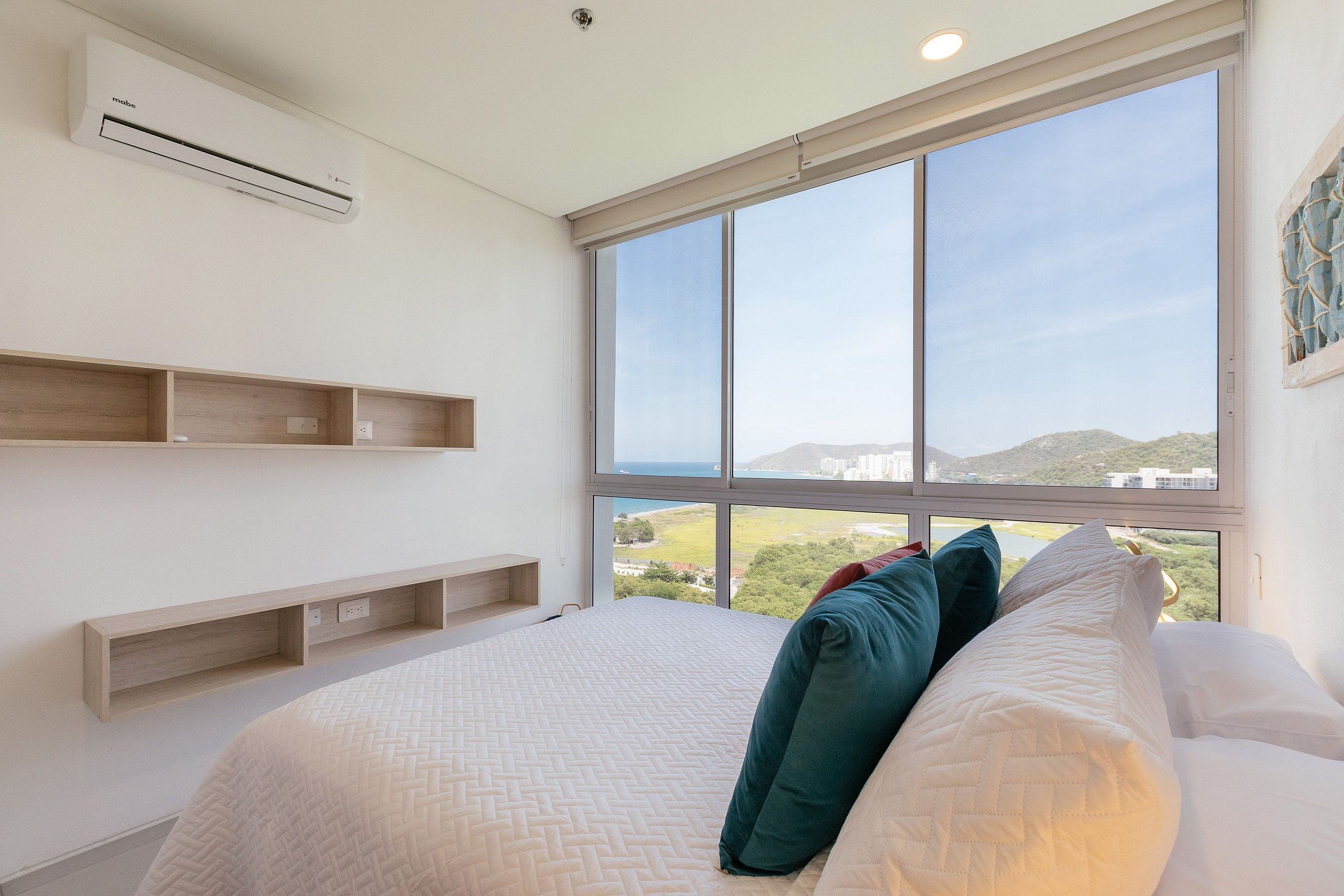 A bedroom with a large window, a bed with pillows, and built-in wooden shelves.