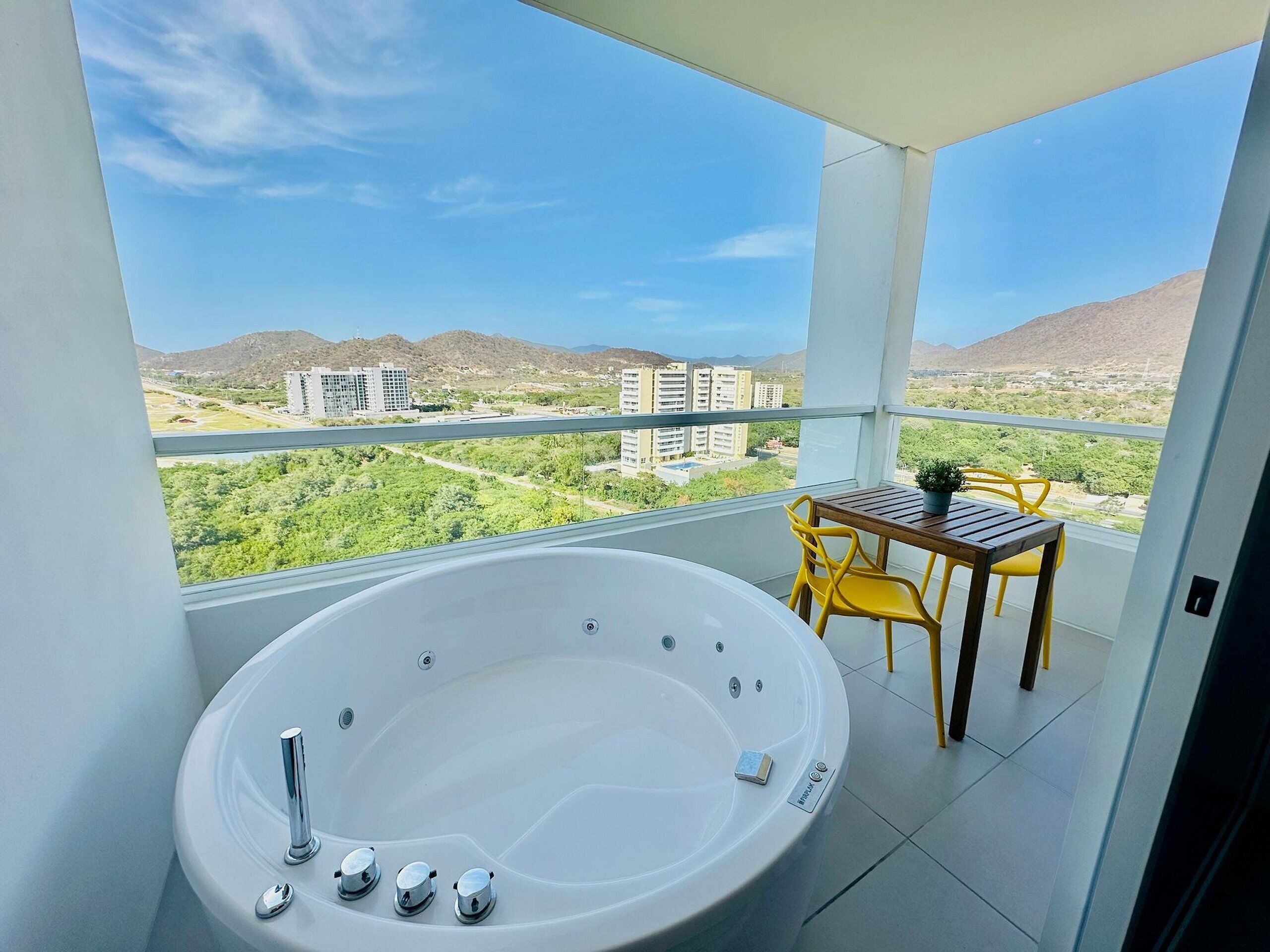 A balcony with a hot tub, yellow chairs, and a table with a potted plant.