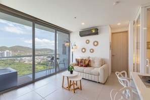 Una sala de estar moderna con un amplio ventanal, un sofá, una mesita y un televisor montado en la pared.
