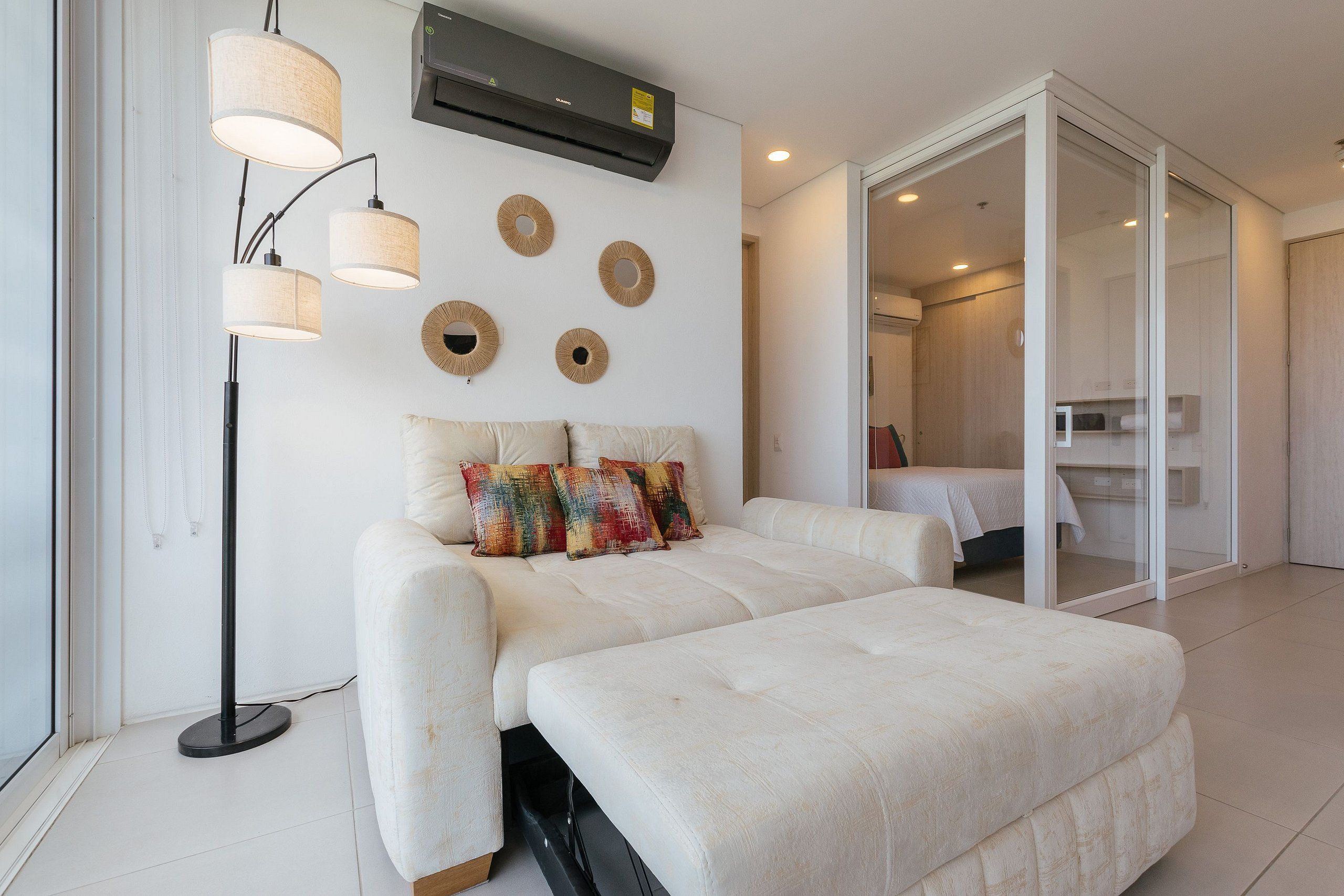 A modern bedroom with a bed, a sofa, a floor lamp, and a mirror.