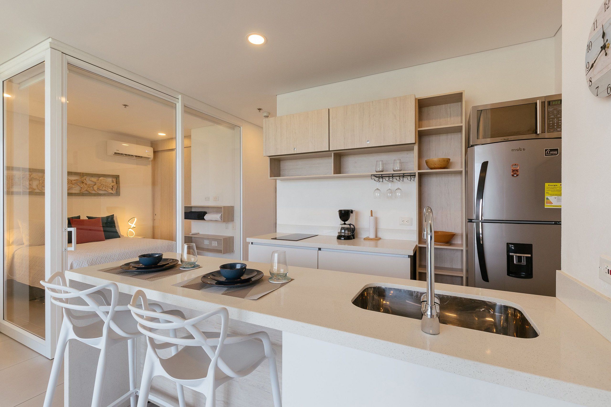 Une cuisine moderne dotée d’un îlot central, d’appareils électroménagers en acier inoxydable et d’un coin repas avec des chaises blanches.