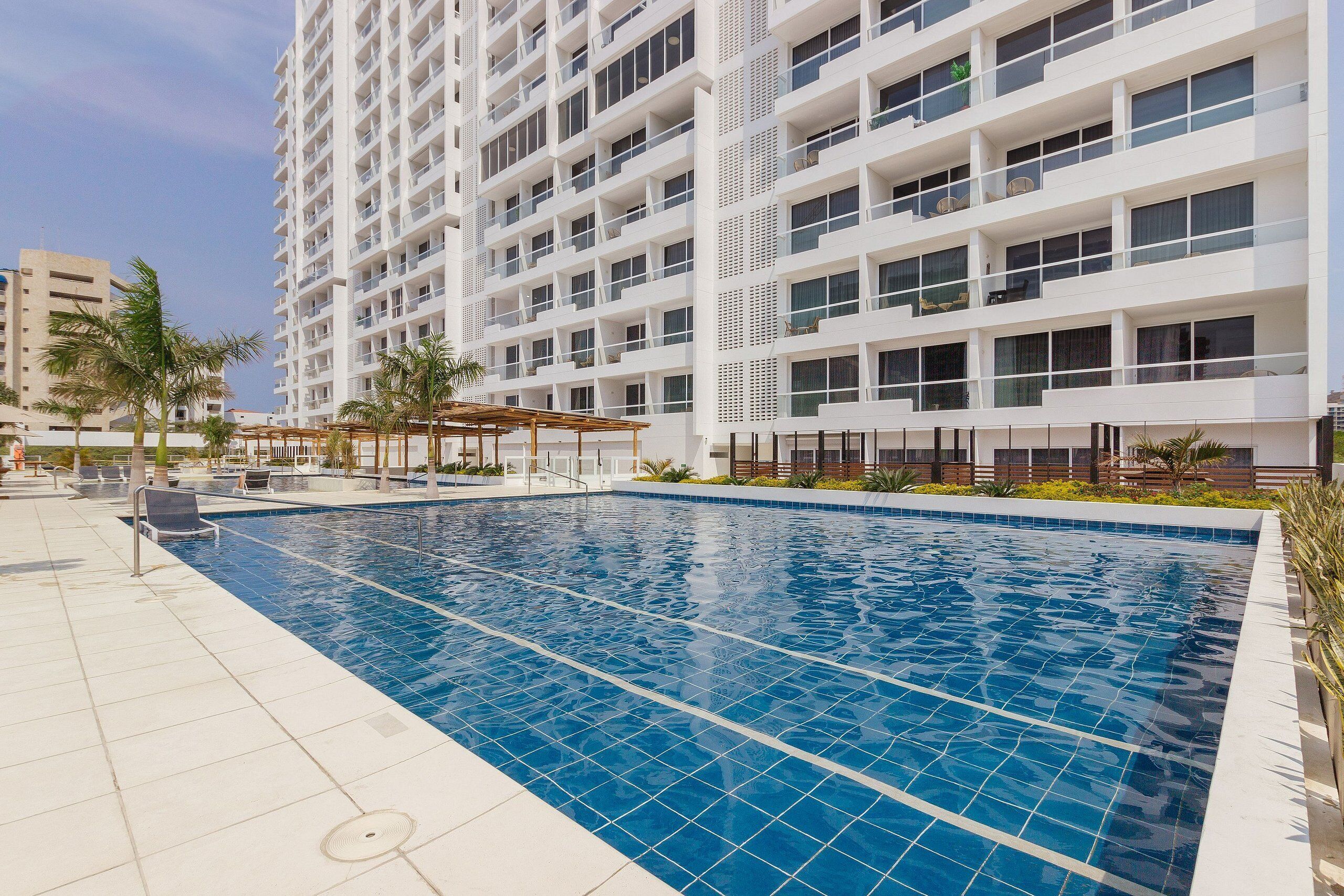A modern hotel with a swimming pool, multiple balconies, and a rooftop terrace.