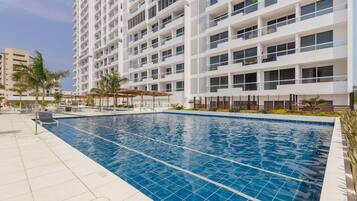 A modern hotel with a swimming pool, multiple balconies, and a rooftop terrace.