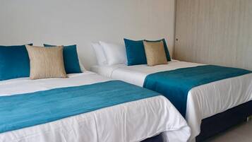 Two single beds with white and teal bedding, a wooden wardrobe, and a plain wall.