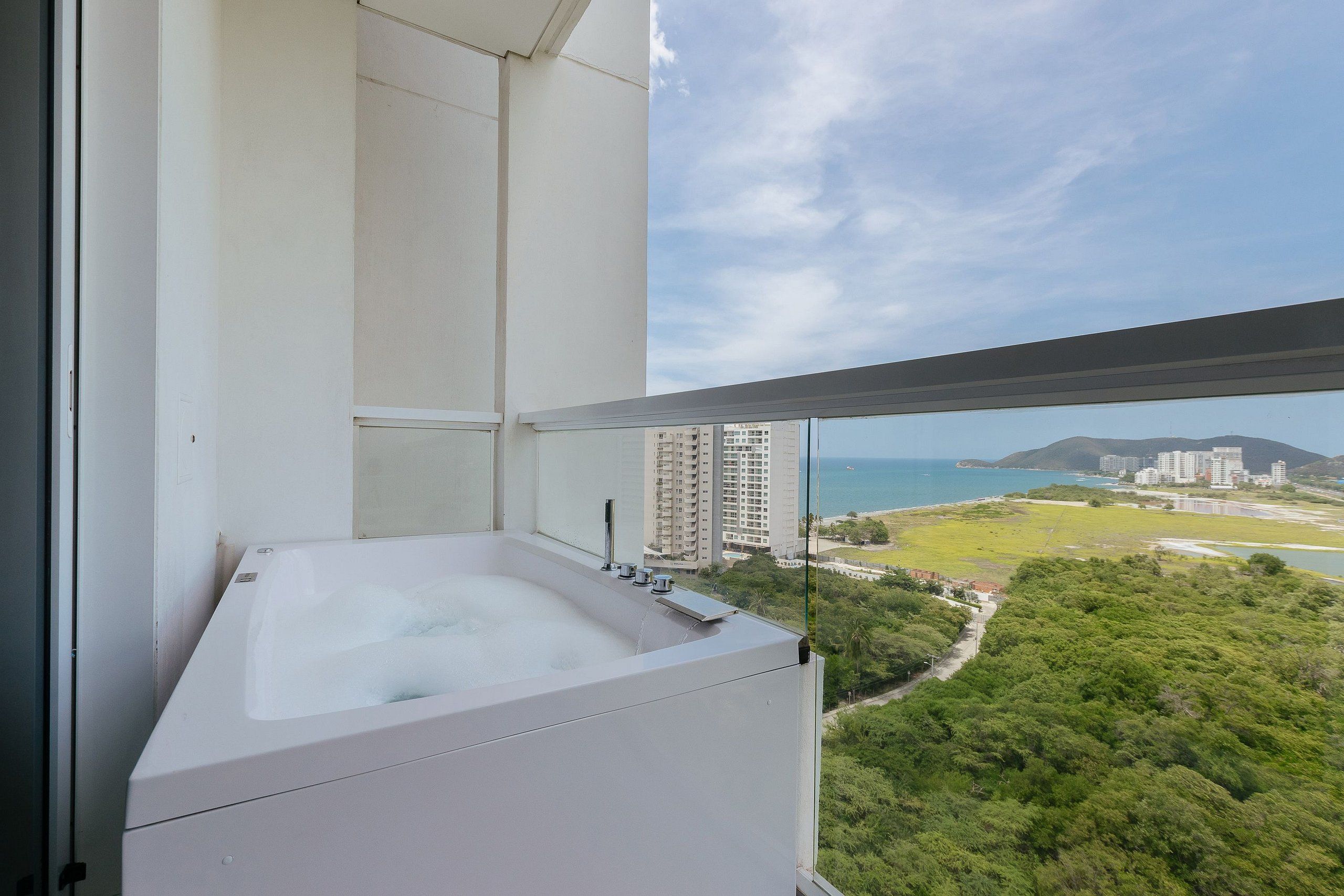 A balcony with a hot tub, overlooking a cityscape and greenery.