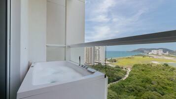 A balcony with a hot tub, overlooking a cityscape and greenery.