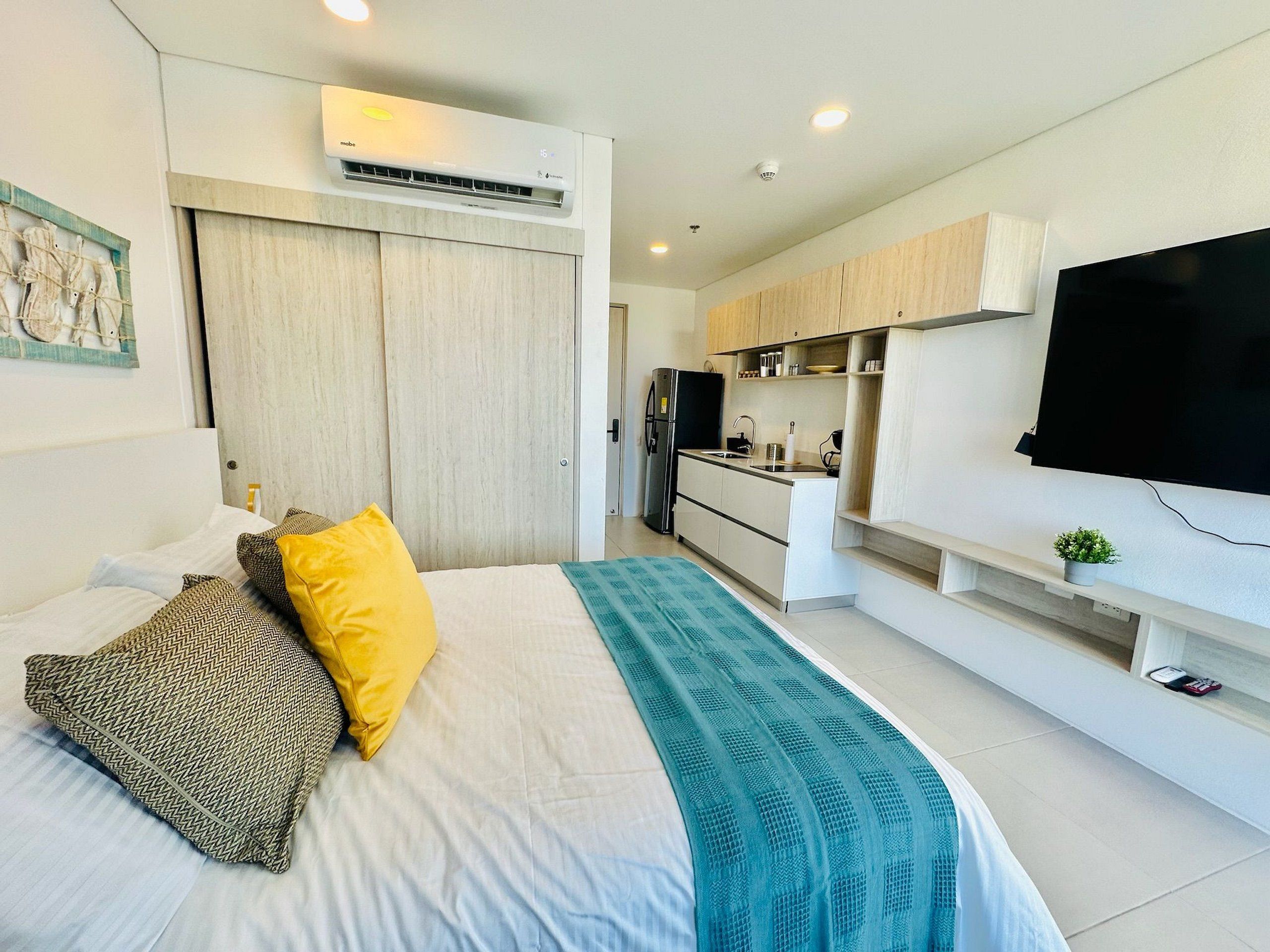 Ein modernes Hotelzimmer mit Bett, Flachbildfernseher, Küchenzeile und Badezimmer.
