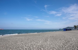 A beach with a clear sky, a red boat in the water, and a blue tent on the sand. - U-GO Porto Horizonte Junto al Mar Sta Mta (Santa Marta)