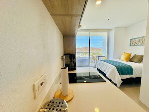 Quarto de hotel com cama, cafeteira, uma mesinha e vista para o exterior.