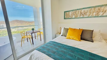 A bedroom with a bed, a balcony with a table and chairs, and a view of the landscape.