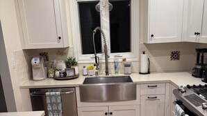 A kitchen with white cabinets, a stainless steel sink, a coffee maker, and a tiled floor.